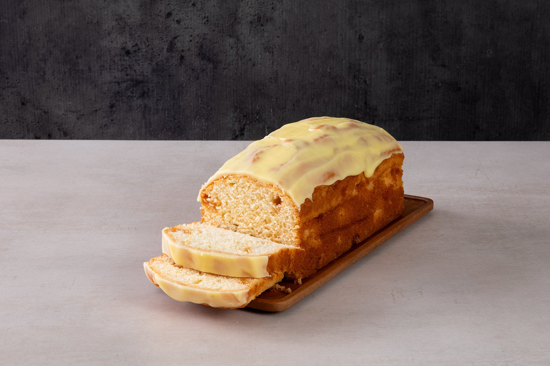 a loaf cake with yellow icing and sliced pieces on a wooden board